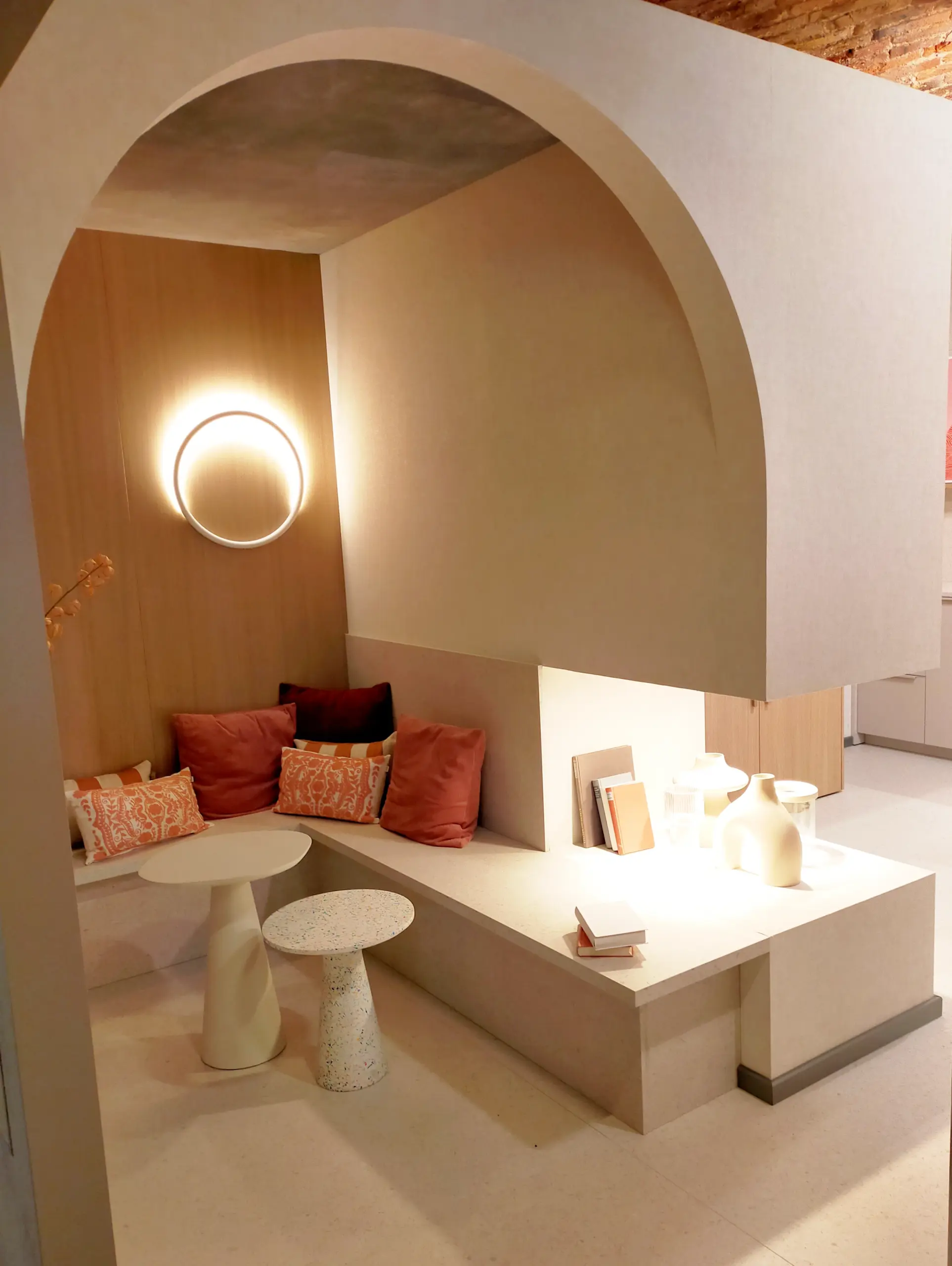 Espace détente architectural : Banquette d'angle intégrée sous une arche design avec éclairage tamisé et tables basses organiques.